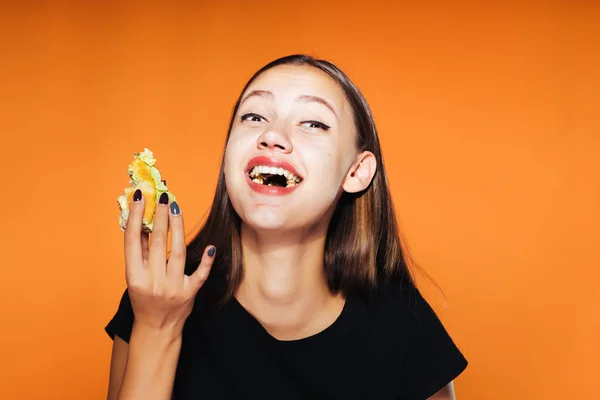 아름 다운 여자 먹는 그녀의 햄버거와 오렌지 배경에 고립 된 귀여운 포옹 — 스톡 사진