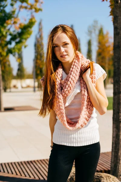 Vacker flicka insvept i en varm halsduk står i parken och ser på kameran. Sunny höstdag — Stockfoto