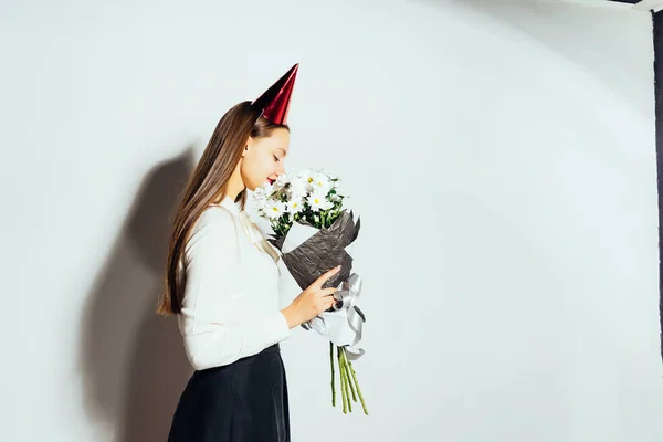 En trevlig tjej med långt hår fick en vacker bukett av chamomiles i födelsedagspresent. en flicka med en festlig mössa — Stockfoto