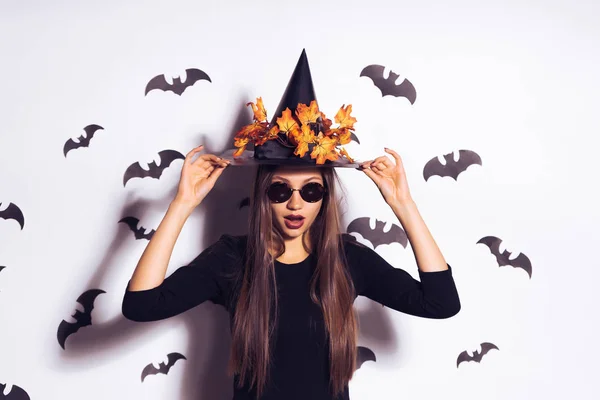 Een mooie heks in een chique zwarte pak, een muts met herfstbladeren en zwarte bril. Tegen de achtergrond van vleermuizen. Breed kunst design van de Halloween party — Stockfoto