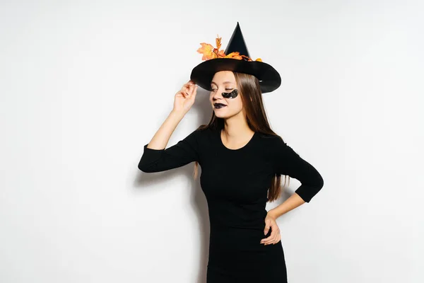 Una mujer de halloween en un vestido de halloween negro y con un sombrero con hojas anaranjadas —  Fotos de Stock