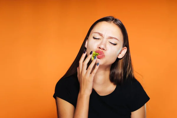 Hladová dívka dychtivě dokončí hamburger, izolované na oranžové pozadí — Stock fotografie
