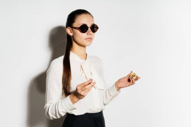 yuvarlak güneş gözlüğü ciddi bir kız bir sikke onun elinde tutan ve uzak görünüyor. Elektronik para. Bitcoins. Kripto para birimi.