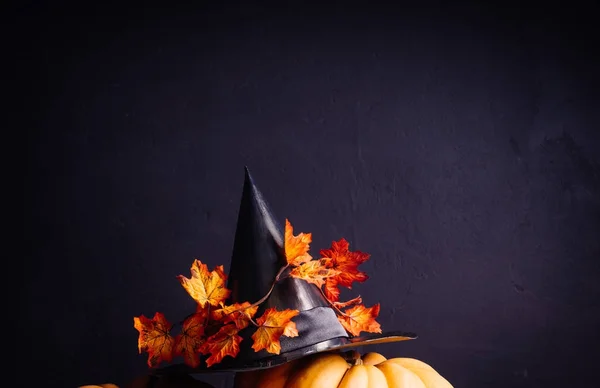 Vedmens Hut auf einem großen Kürbis getragen. Vorbereitungen für den Feiertag Halloween. auf schwarzem Hintergrund. Hut mit abgefallenen Blättern — Stockfoto