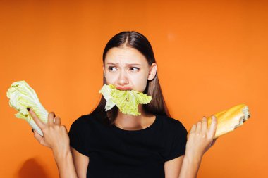 Kız bir lahana ve bir somun onun elinde tutar. Lahana, turuncu zemin üzerine izole çiğneme kız