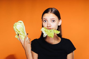 Kız ne yazık ki lahana kemikleri ve onun elinde tutar. Turuncu bir arka plan üzerinde izole. Taze sebze, diyet
