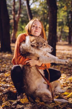 Sevimli bir kız köpeğini hugs ve doğrudan fotoğraf makinesine benziyor. Düşen yapraklar, sıcak bir sonbahar günü.