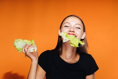 Kız hevesle lahana yiyor. Güzel vücut, doğru beslenme, sağlıklı gıda, beslenme, taze sebze. Turuncu zemin üzerine izole.