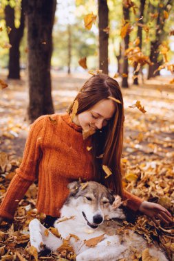 güzel kız köpeğiyle düşen sonbahar yaprakları üzerinde yatıyor. Sıcak hava, sonbahar günü, yaprakları düşüyor