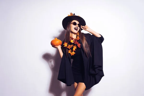 Piękna dziewczyna halloween szalony z długie włosy. Halloween Kobieta w czarnej sukience halloween i w kapeluszu z liści pomarańczy. — Zdjęcie stockowe
