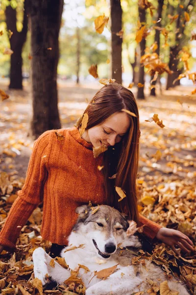 A menina encantadora encontra-se em folhas caídas do outono com seu cão. Tempo quente, dia de outono, folhas caindo — Fotografia de Stock