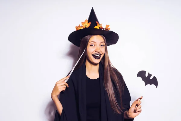 Halloween heks lacht en heeft een toverstokje en vleermuis in handen. Het meisje gaat naar een Halloween-feest. — Stockfoto