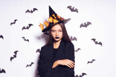 siyah bir Cadılar Bayramı şapka ve siyah yarasalar ile beyaz bir duvar siyah ruj tezgahı ile üzgün. Gotik kız