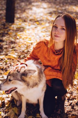 Kızıl saçlı genç kız ile onun büyük köpek, düşen sonbahar yaprakları etrafında bir parkta oturuyor,