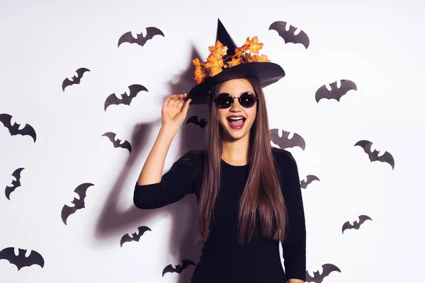 행복 한 어린 소녀는 검은 마녀 할로윈 모자에에서 검은 박쥐와 흰 벽에 서 — 스톡 사진