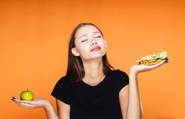 Aç bir kız bir diyet, bir elma ve zararlı sandviç tutarak oturuyor