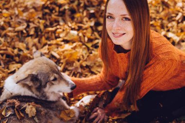 Kızıl saçlı kız düşmüş sonbaharda köpeğiyle oturuyor, gülümseyen ve poz bırakır