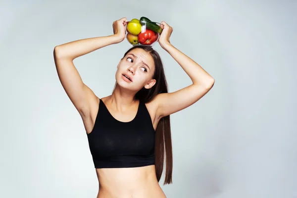 Uma jovem atlética parece chateada, segura um prato com vegetais úteis e frutas sobre a cabeça — Fotografia de Stock