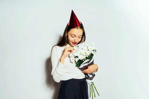 Lycklig flicka i festlig mössa som håller en bukett av vita blommor i händer — Stockfoto