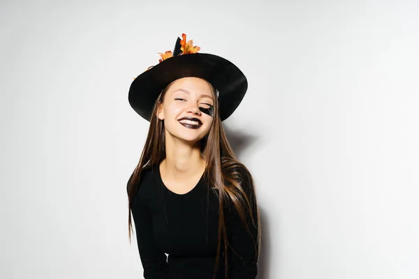 A young laughing gothic girl in a black witch hat rejoices in halloween — Stock Photo, Image