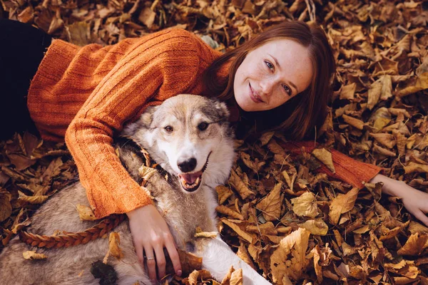 güzel kızıl saçlı kız köpeğiyle düşmüş sonbahar yığını içinde poz bırakır