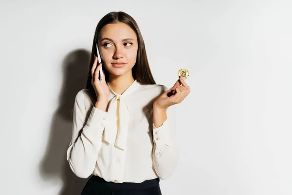 Jovem mulher de negócios falando ao telefone, segurando um bitcoin de ouro em sua mão, estudando criptomoeda — Fotografia de Stock