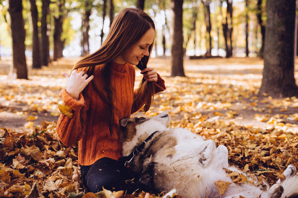 young red-haired laughing girl playing with her dog in a pile of fallen gold leaves
