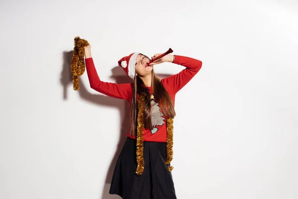 Joven feliz chica celebra el Año Nuevo y la Navidad, en una gorra roja, suéter festivo y oropel de oro — Foto de Stock