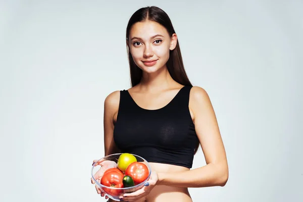 En ung smal tjej klockor sin figur, innehar en tallrik med användbar grönsaker och frukter i händerna — Stockfoto