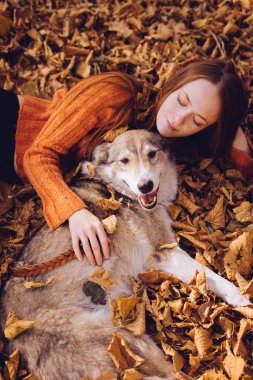 Kızıl saçlı bir kız bir düşen sonbahar yaprakları köpeği ile birlikte yatıyor.