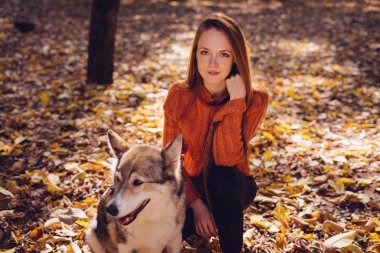 Kızıl saçlı bir kız bir düşen sonbahar yaprakları köpeğini birlikte oturur.