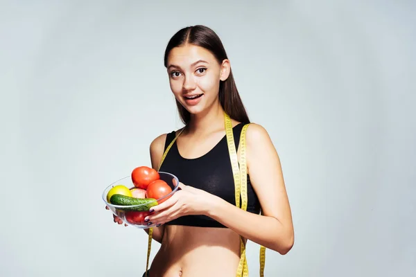 Спортивная девушка наблюдает за своей фигурой, держа тарелку с полезными овощами и фруктами — стоковое фото
