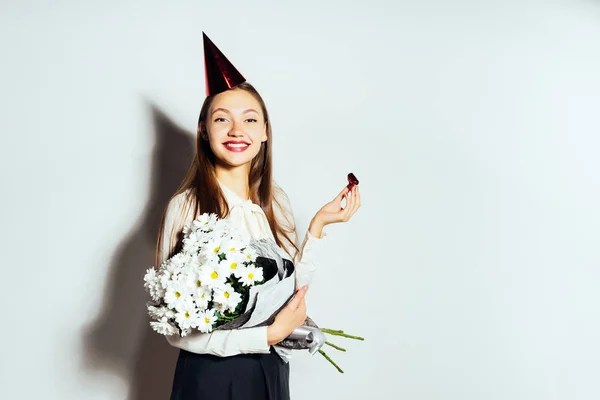 Een jong meisje in een rode feestelijke hoed houdt een groot boeket van witte bloemen — Stockfoto