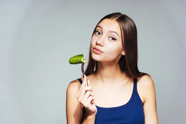 Una joven con un top azul sentada a dieta y comiendo un pepino bajo en calorías — Foto de Stock