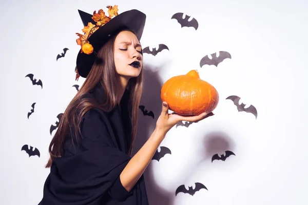 Een gotische meisje in de vorm van een heks in halloween, houdt een oranje pompoen in haar hand — Stockfoto