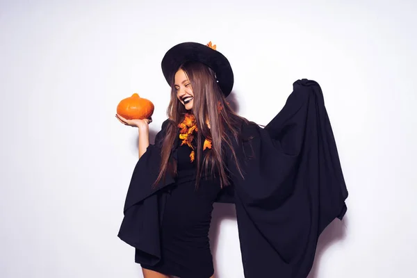 Jong lachen gotische meisje in het beeld van een heks in halloween, een pompoen met in haar hand — Stockfoto
