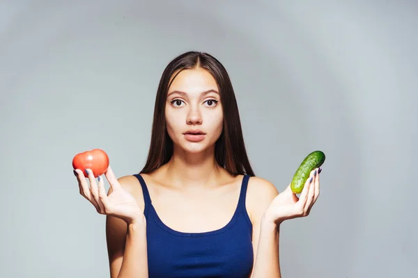 Ung flicka sitter på en diet, håller i händerna en användbar gurka och tomat — Stockfoto