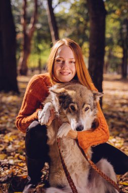 Kızıl saçlı genç kız köpeğini sonbahar düşmüş yaprak yığını ile oynuyor