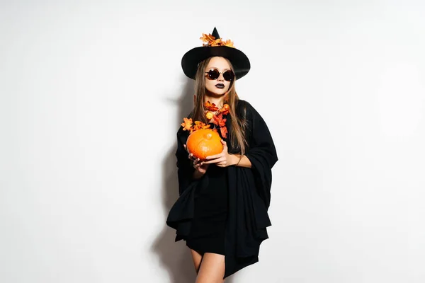 Jeune fille sexy souriante en forme de sorcière à Halloween, tenant une citrouille dans les mains — Photo