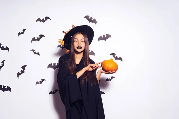 Jonge lachende sexy meisje in de vorm van een heks in halloween, bedrijf van een pompoen in handen — Stockfoto