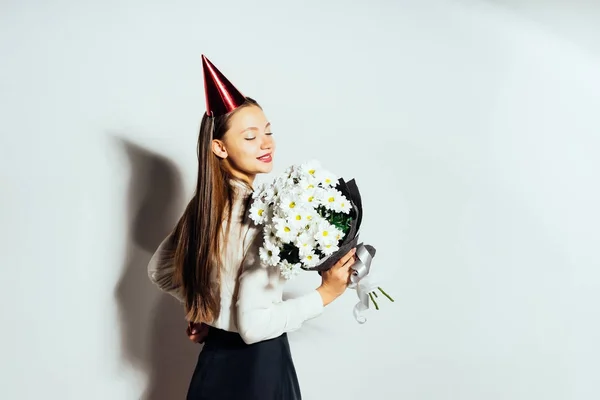 Sorrindo menina feliz celebrando algo, em um boné vermelho e com um buquê de flores brancas — Fotografia de Stock