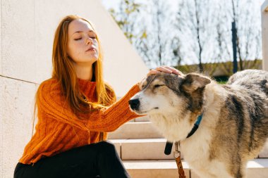 Kızıl saçlı güzel kız merdivende oturup onu büyük köpek ile oynuyor