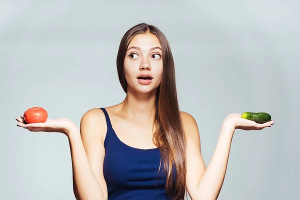 En ung atletisk flicka klockor sin figur, innehar en gurka och en tomat i händerna — Stockfoto