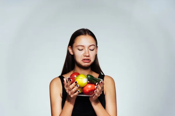 Egy fiatal sportos lány figyeli alakját, a lemez hasznos zöldségek és gyümölcsök tart a kezében — Stock Fotó
