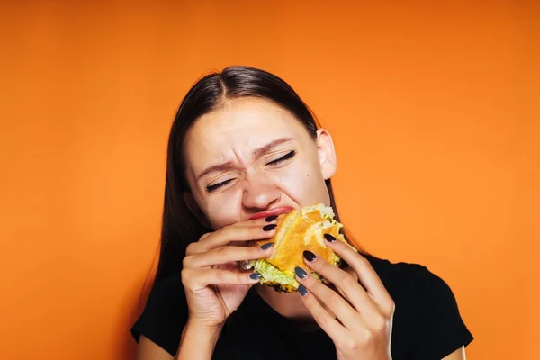 Голодная девушка хочет сбросить вес, но охотно ест вредный бургер — стоковое фото