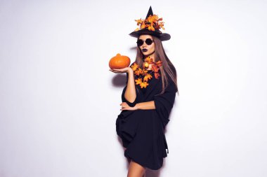 Cadı kız Cadılar bayramı kıyafeti bir partiye gidiyor ve bir kabak, siyah şapka, yarasalar arka planda tutan