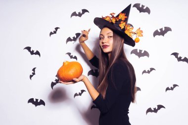 Cadı kız Cadılar bayramı kıyafeti bir partiye gidiyor ve bir kabak, siyah şapka, yarasalar arka planda tutan