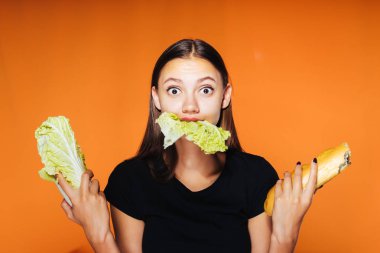 Aç bir kız lahana yemek yiyor ve açgözlü gözlerle kameraya bakıyor. Kız bir lahana ve bir somun ekmek tutuyor. Turuncu bir arka plan üzerinde izole.
