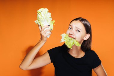 Kız bir diyet lahana iştahla yiyor. Güzel şekil, sağlıklı gıda, turuncu zemin üzerine izole.