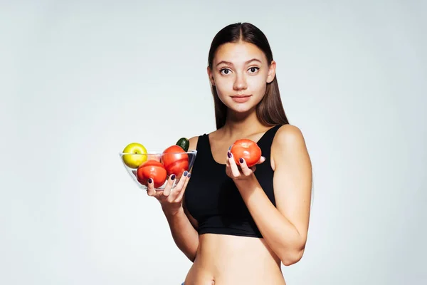 Unga vackra sportig tjej klockor sin figur, innehar en tallrik med användbar grönsaker och frukter i händerna — Stockfoto